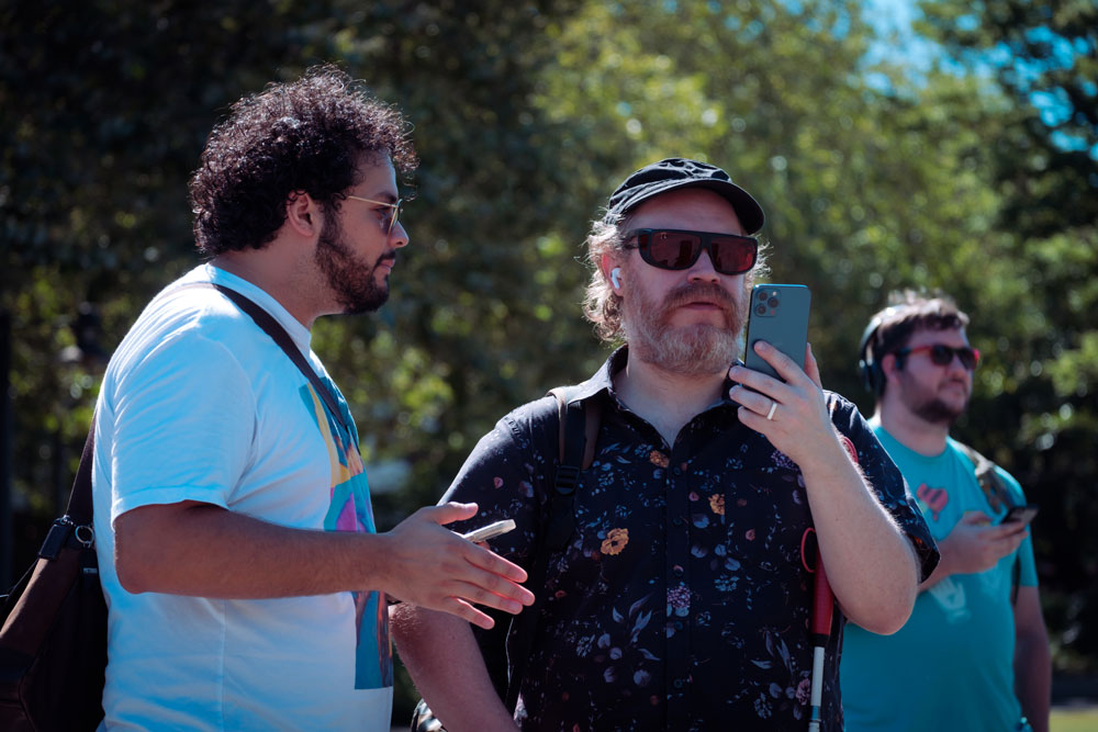Author Andy Slater testing Space-Time Adventure Tours while holding his phone in front of him, Julian Ochoa standing next to him, talking.
